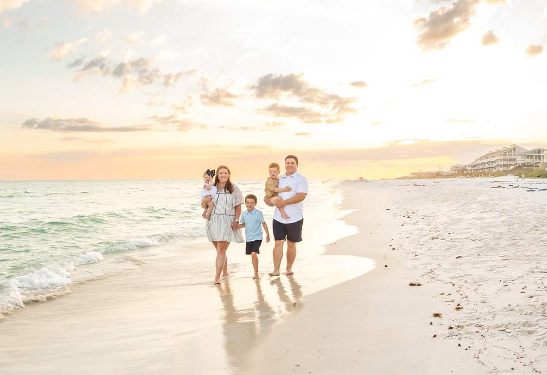 Kyle, his wife and their three children walking along the shoreline at sunset